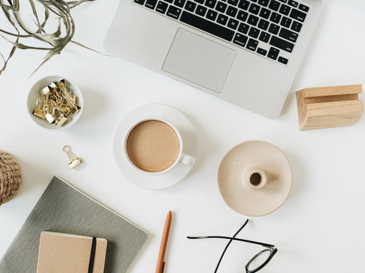 flatlay image of computer, coffee mug, eye glasses, and note pads