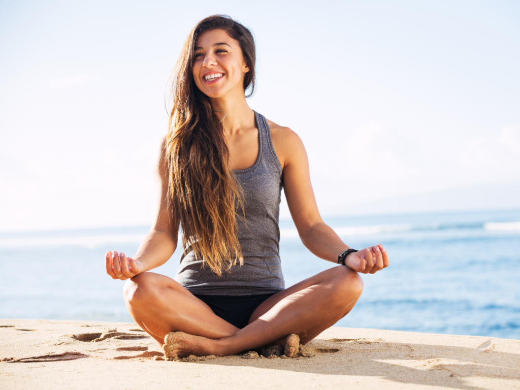 A woman meditating outside on the beach in the sunlight 