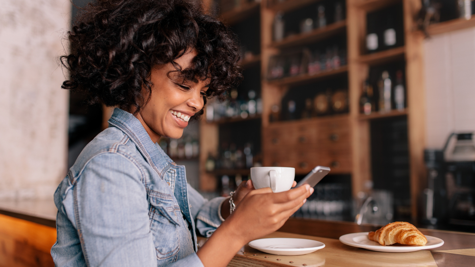 Woman smiling looking at  her phone with coffee in other hand