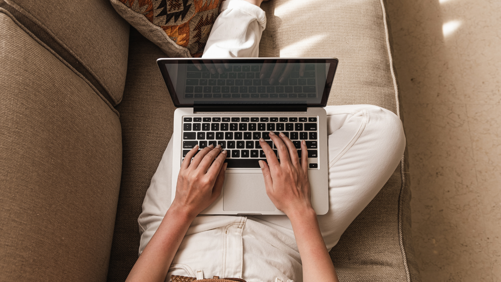 Woman's hands typing on laptop while laying on a couch